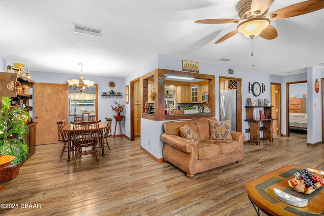 living room with ceiling fan with notable chandelier, a textured ceiling, and light hardwood / wood-style floors