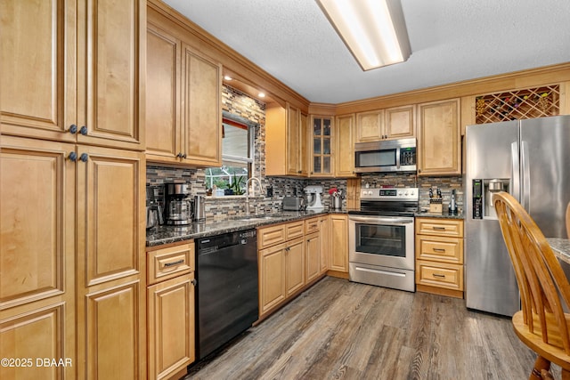 kitchen featuring wood-type flooring, decorative backsplash, sink, stainless steel appliances, and dark stone counters