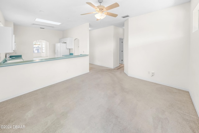 unfurnished living room with ceiling fan, light colored carpet, and sink