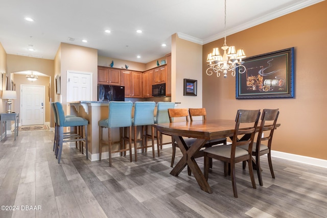 dining area with wood-type flooring, an inviting chandelier, and ornamental molding