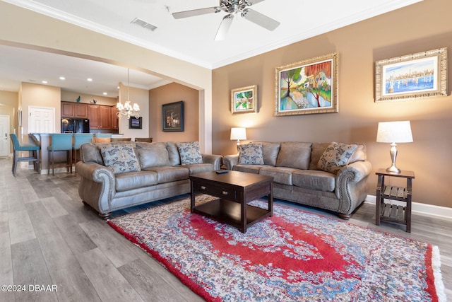 living room with ceiling fan with notable chandelier, ornamental molding, and light hardwood / wood-style flooring