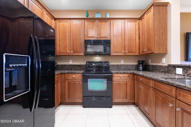 kitchen with dark stone counters, light tile patterned floors, and black appliances