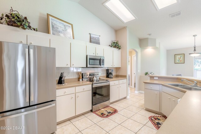 kitchen featuring light tile patterned flooring, stainless steel appliances, hanging light fixtures, sink, and white cabinets