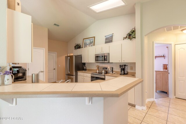 kitchen featuring stainless steel appliances, white cabinetry, a breakfast bar, kitchen peninsula, and vaulted ceiling