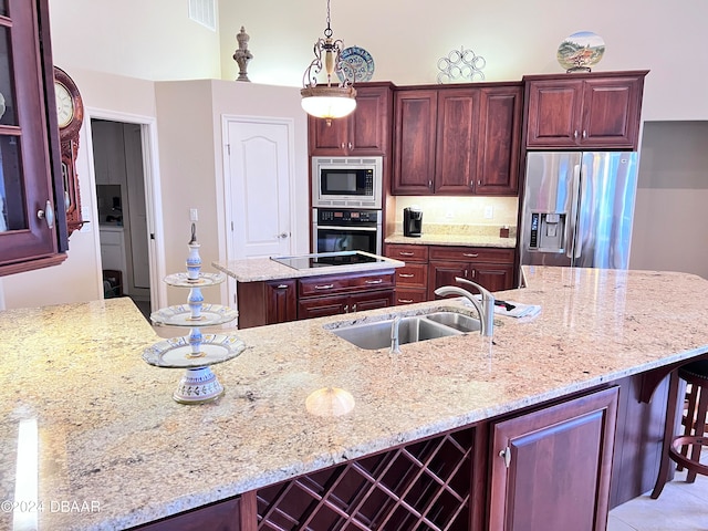 kitchen with appliances with stainless steel finishes, sink, hanging light fixtures, light stone counters, and a center island with sink