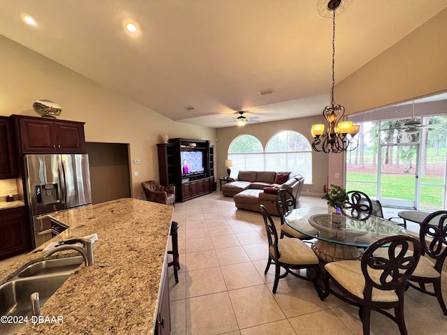 tiled dining area with sink, ceiling fan with notable chandelier, and high vaulted ceiling