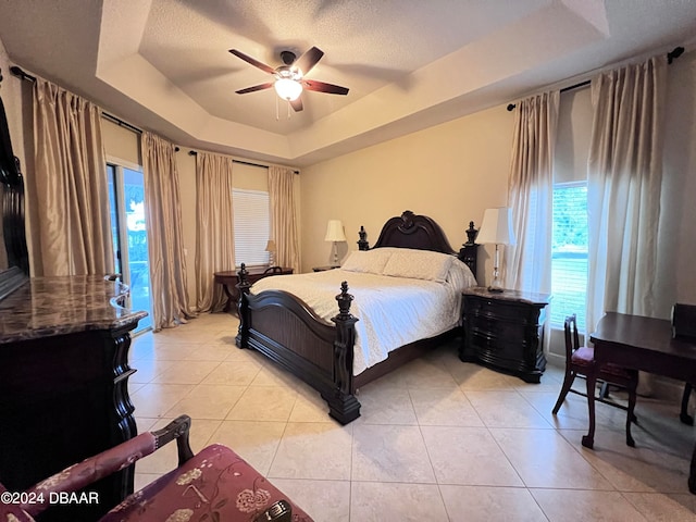 bedroom with light tile patterned floors, a raised ceiling, a textured ceiling, and ceiling fan