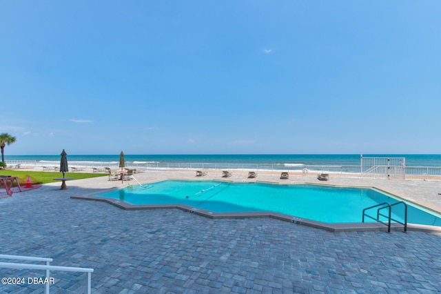 view of swimming pool featuring a patio area, a water view, and a view of the beach