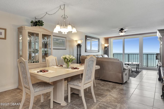 tiled dining space featuring ceiling fan with notable chandelier, a water view, and a textured ceiling