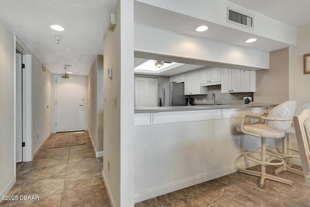 kitchen featuring sink, kitchen peninsula, stainless steel fridge with ice dispenser, and white cabinets