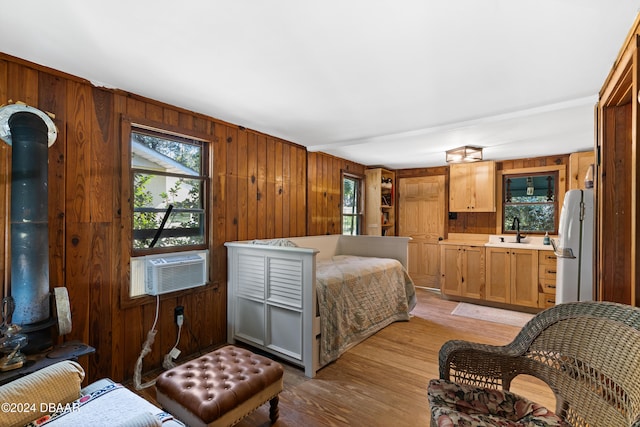 bedroom featuring wood walls, cooling unit, white refrigerator, sink, and light hardwood / wood-style flooring