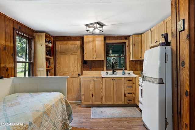 kitchen with wood walls, light wood-type flooring, white appliances, and sink