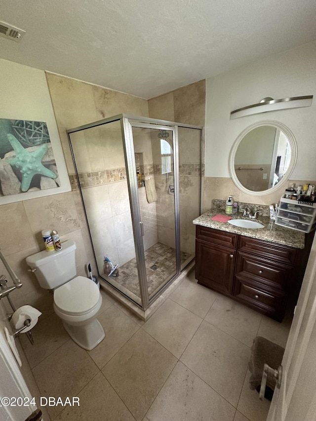 bathroom featuring vanity, tile patterned floors, toilet, tile walls, and a shower with shower door