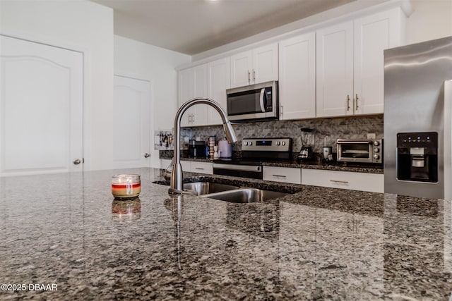 kitchen with sink, white cabinetry, appliances with stainless steel finishes, dark stone counters, and backsplash