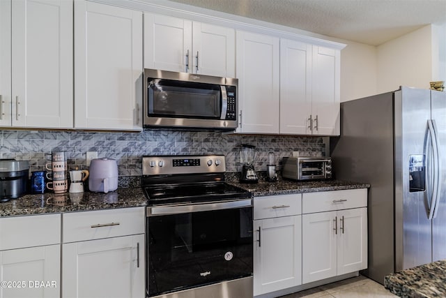 kitchen with white cabinetry, appliances with stainless steel finishes, dark stone countertops, and decorative backsplash