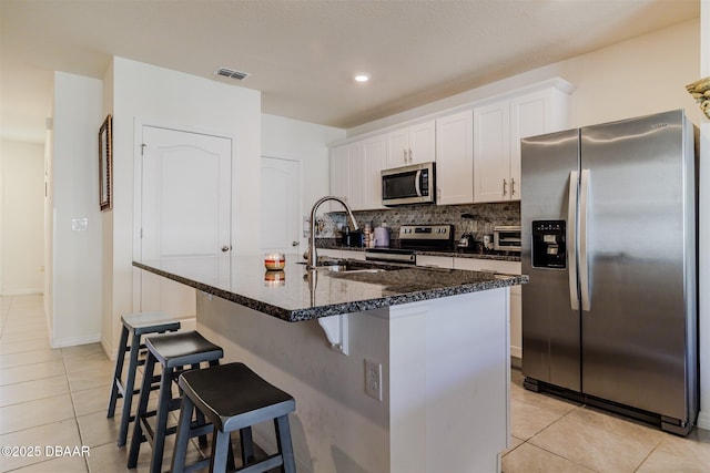 kitchen featuring stainless steel appliances, light tile patterned floors, a center island with sink, and white cabinets