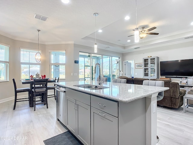 kitchen featuring light stone counters, a center island with sink, light wood-type flooring, hanging light fixtures, and ceiling fan