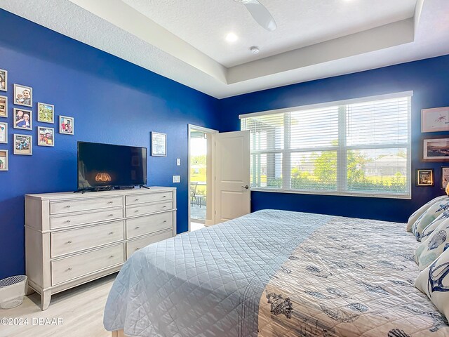 bedroom with light hardwood / wood-style floors, ceiling fan, a textured ceiling, and a raised ceiling