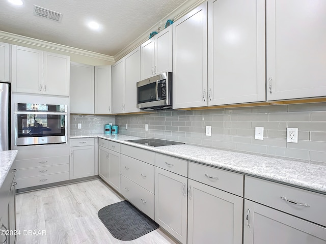 kitchen featuring stainless steel appliances, light stone counters, a textured ceiling, backsplash, and light wood-type flooring