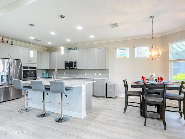 kitchen featuring a kitchen island with sink, appliances with stainless steel finishes, hanging light fixtures, and gray cabinetry