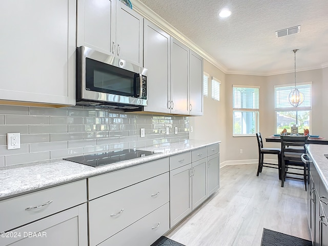 kitchen featuring tasteful backsplash, decorative light fixtures, ornamental molding, and black electric stovetop