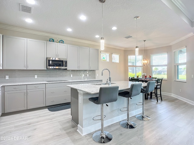 kitchen featuring ornamental molding, pendant lighting, sink, a breakfast bar, and a kitchen island with sink