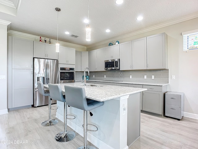 kitchen with sink, appliances with stainless steel finishes, decorative light fixtures, an island with sink, and crown molding