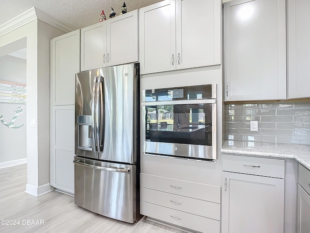 kitchen with tasteful backsplash, white cabinetry, appliances with stainless steel finishes, a textured ceiling, and light wood-type flooring