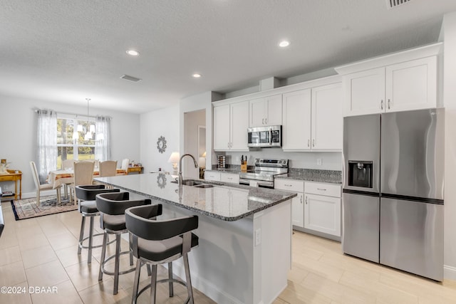 kitchen featuring an island with sink, stainless steel appliances, a kitchen bar, white cabinetry, and a sink