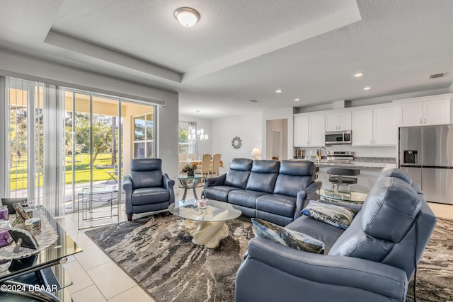 living room featuring light tile patterned floors, a textured ceiling, a raised ceiling, and a notable chandelier