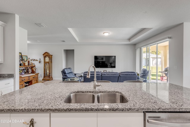 kitchen featuring light stone countertops, a textured ceiling, white cabinetry, and sink