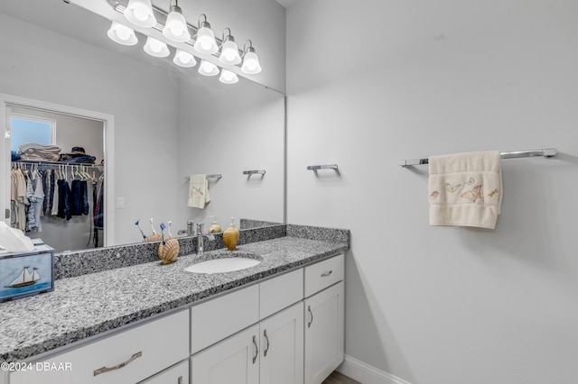 bathroom with a walk in closet, vanity, and baseboards