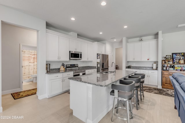 kitchen with stone counters, a center island with sink, white cabinets, appliances with stainless steel finishes, and a kitchen bar