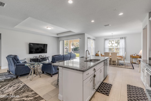 kitchen with stainless steel dishwasher, stone countertops, open floor plan, white cabinets, and a sink