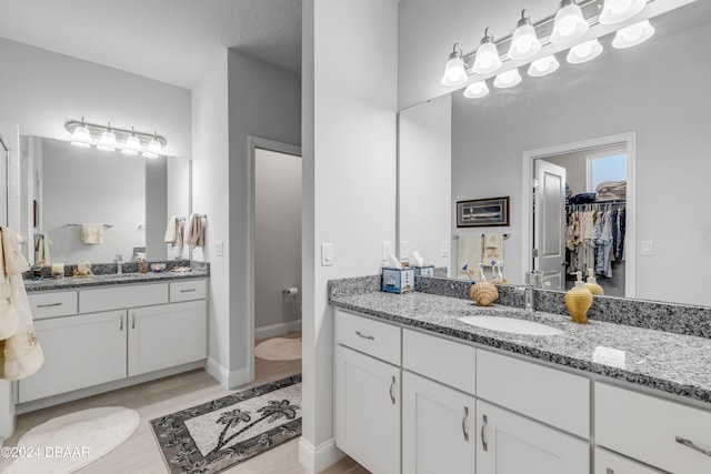 full bath with a spacious closet, wood finished floors, two vanities, and a sink