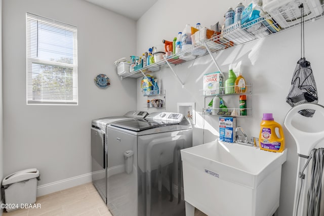 clothes washing area featuring light tile patterned flooring, laundry area, a sink, baseboards, and washing machine and clothes dryer