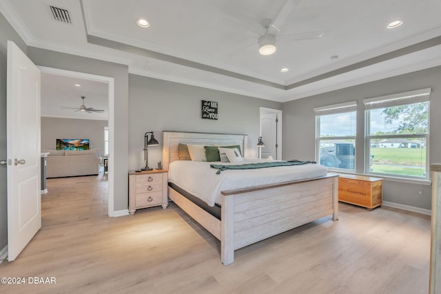 bedroom featuring light wood-type flooring, a raised ceiling, ceiling fan, and crown molding