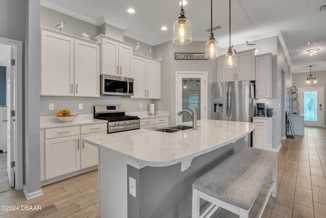 kitchen with hanging light fixtures, sink, appliances with stainless steel finishes, and an island with sink