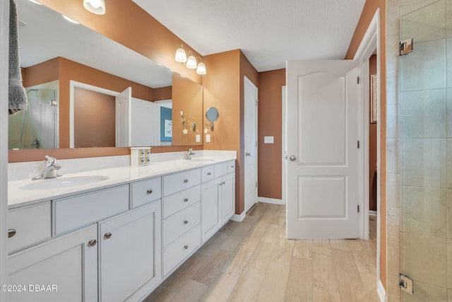 bathroom featuring vanity, wood-type flooring, a shower with door, and a textured ceiling