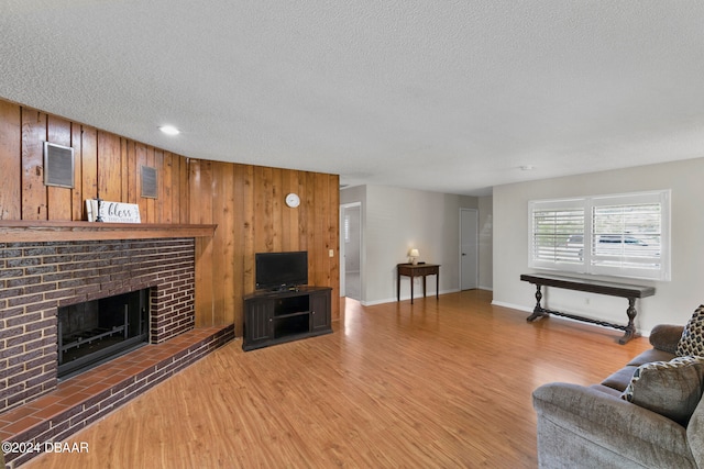 living room featuring a textured ceiling, wood walls, wood-type flooring, and a brick fireplace