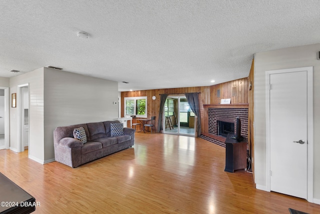 living room with wooden walls, a textured ceiling, light hardwood / wood-style floors, and a brick fireplace