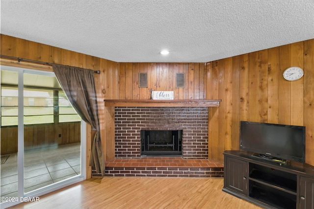 unfurnished living room with a fireplace, wood walls, a textured ceiling, and light hardwood / wood-style flooring