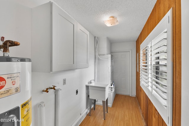 washroom with electric water heater, light hardwood / wood-style floors, and a textured ceiling