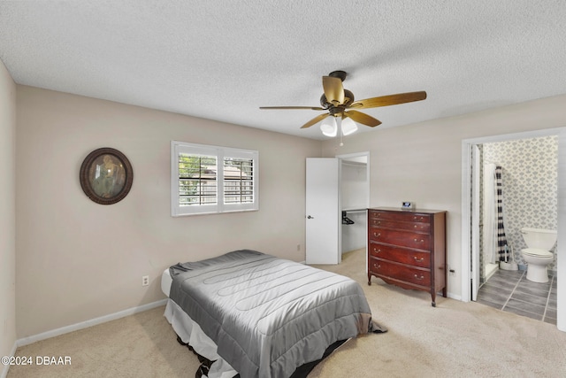 bedroom featuring a textured ceiling, light colored carpet, ceiling fan, and ensuite bath