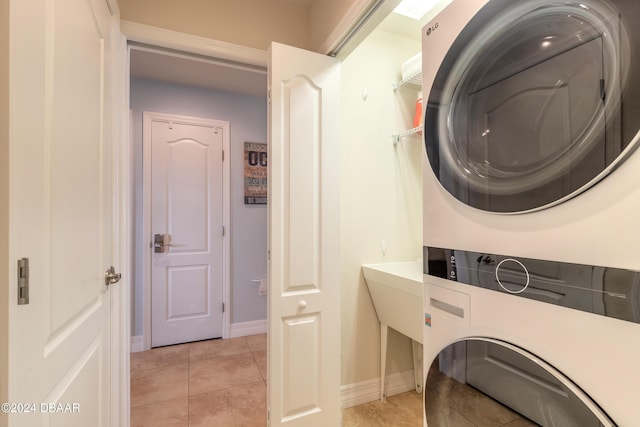 washroom featuring light tile patterned floors, stacked washer / dryer, laundry area, and baseboards