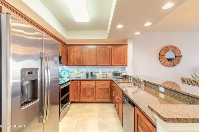 kitchen featuring light stone counters, stainless steel appliances, backsplash, sink, and kitchen peninsula