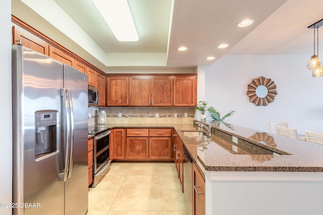 kitchen with a peninsula, brown cabinets, appliances with stainless steel finishes, and a sink