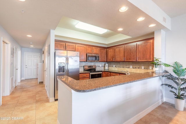 kitchen with stainless steel appliances, tasteful backsplash, a peninsula, and brown cabinetry