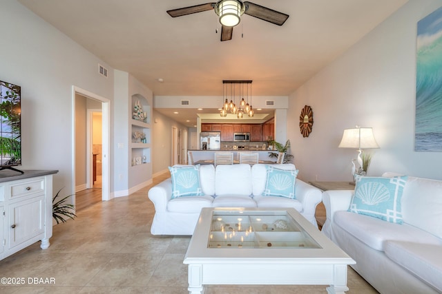 living room with built in features, ceiling fan with notable chandelier, visible vents, and baseboards