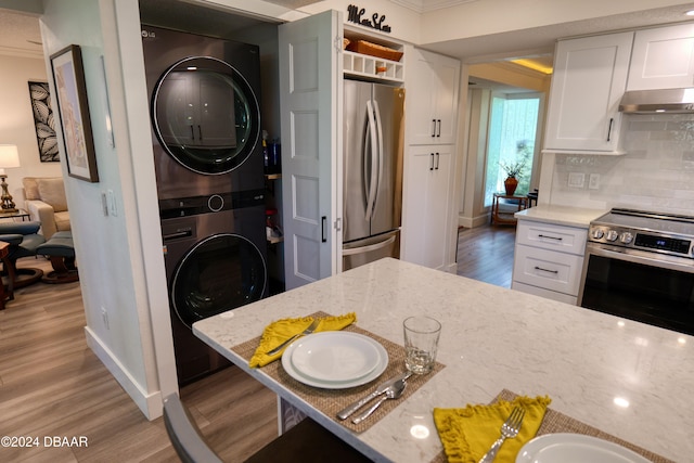 kitchen featuring light stone countertops, light wood-type flooring, white cabinetry, stacked washer / dryer, and stainless steel appliances